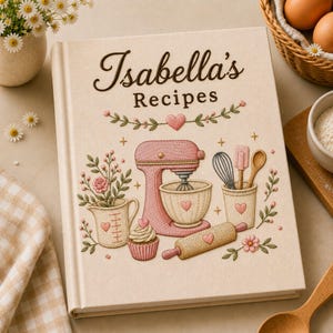 May include: A cream-coloured hardback recipe book titled Isabella's Recipes, featuring embroidered-style illustrations of a pink stand mixer, a measuring cup with flowers, a cupcake, a rolling pin, and kitchen utensils, all accented with small hearts.