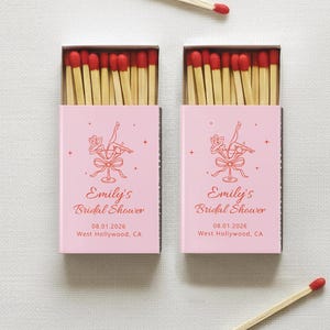 May include: Two pink matchboxes with red-tipped matches and the text "Emily's Bridal Shower" are displayed. The boxes have a decorative illustration and the date 08.01.2026. Two loose matches are also visible.