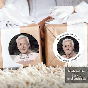 May include: Two wrapped gifts with white ribbon and round stickers. The stickers feature a portrait of a man with the text "In Loving Memory of Lucas Reed 1950-2025" and "In Memory of Lucas Reed 1952-2025". The image also includes the text "Made in USA Easy to peel and stick".