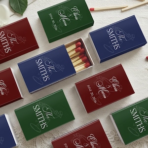May include: An assortment of personalized matchboxes in various colors, including red, green, and blue. Each box features the text "The Smiths" and a decorative cocktail glass design. Some boxes also include names and a date.