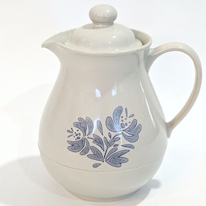 May include: A white ceramic pitcher with a blue floral design. The pitcher has a lid and a handle.