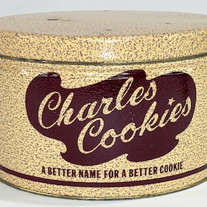 May include: A vintage yellow and brown tin cookie container with the text "Charles Cookies" in a red cursive font and the tagline "A Better Name For A Better Cookie".