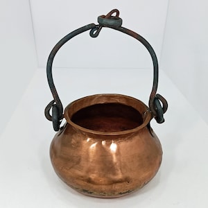 May include: A small copper pot with a hammered finish and a rustic iron handle. The pot has a rounded body and a wide opening.
