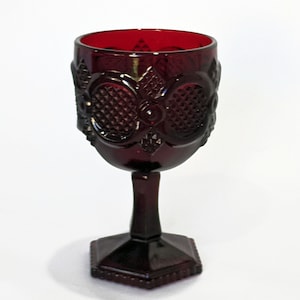 May include: A deep red glass goblet with a hexagonal base and intricate diamond-shaped patterns. The goblet has a wide bowl and a tall stem.