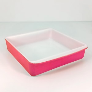 May include: A square baking dish with a bright pink exterior and a white interior. The dish has a simple, clean design, perfect for baking casseroles, brownies, or other treats. The dish is empty and ready for use.