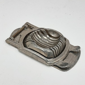 May include: A silver egg slicer with a hinged design. The slicer has a series of blades that cut the egg into even slices.