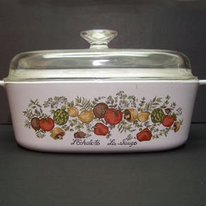 May include: White oval casserole dish with a glass lid. The dish has a floral design with vegetables and mushrooms. The text "L'Echalote La Sauge" is printed on the bottom of the dish.