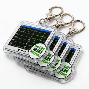 May include: Clear acrylic keychains featuring a medical monitor design with a green EKG readout. Each keychain has a silver clasp and a white and green circular graphic that reads "I'VE GOT GREAT RHYTHM!"