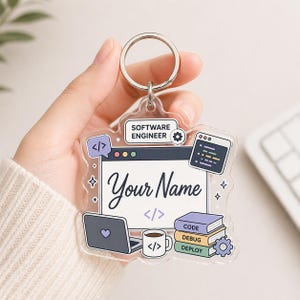 May include: A clear acrylic keychain with a silver ring. The keychain features a software engineer theme with a laptop, coffee cup, books, and the text "Your Name". Additional text includes "SOFTWARE ENGINEER", "CODE", "DEBUG", and "DEPLOY".