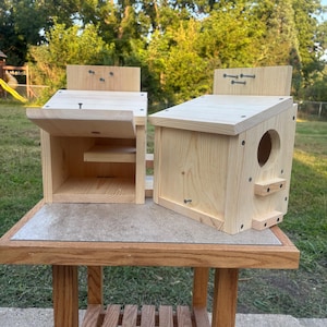 May include: Two light-colored wooden birdhouses with slanted roofs. One birdhouse is open, revealing an interior shelf, while the other is closed and features a circular entrance hole and a small perch below the opening. Both are constructed from pine.