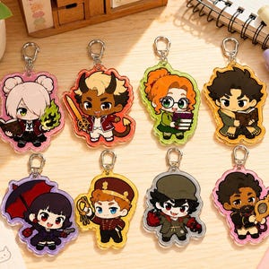 May include: Eight acrylic keychains featuring chibi-style characters with diverse designs, including figures holding books, a sword, an umbrella, keys, and a mirror. Each keychain has a silver-toned metal lobster clasp attached to the top.