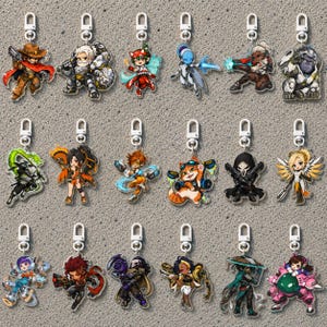 May include: A collection of eighteen acrylic keychains featuring colorful chibi-style illustrations of various characters, each equipped with a silver-toned lobster clasp attachment for hanging, arranged in three rows of six individual pieces.