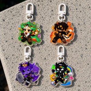 May include: Four acrylic keychains featuring chibi-style characters with white plastic swivel clasps. The top left shows a green-haired explorer, top right a fire-themed character, bottom left a purple demon with a shield, and bottom right a black figure with a rainbow.