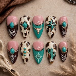 May include: A set of ten almond-shaped press-on nails featuring a mix of cow print, solid pink, and teal designs. Embellishments include turquoise-coloured stones, a gold-toned bull skull, a starburst, and a cactus motif with white painted accents.