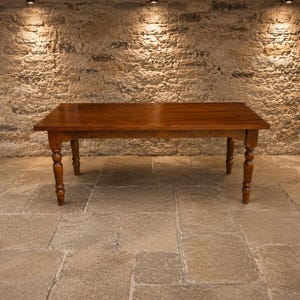May include: A rectangular wooden dining table with a smooth, polished brown surface and four turned legs. The table features a solid wood construction with a warm, medium-toned finish, showcasing a clean, flat top and sturdy, rounded support posts.