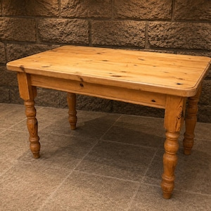 May include: A rectangular wooden table with a light brown finish and visible wood grain patterns. The table features a smooth, flat top surface with rounded corners and four sturdy, turned legs with a decorative, rounded spindle design.
