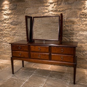 May include: A dark wood vanity table featuring a tri-fold mirror assembly and six drawers arranged in two horizontal rows. Each drawer is equipped with a circular metal pull. The piece stands on four tapered legs and has a polished finish.