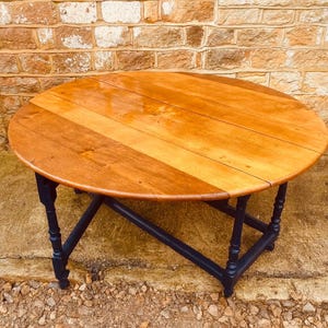May include: A circular wooden table with a light brown surface and dark blue legs. The tabletop is constructed from wooden planks. The legs are intricately designed and support the table. The table is a classic piece of furniture, with a diameter of approximately 90 cm.