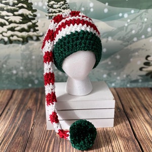 May include: A green, white and red striped elf hat with a long, green, white and red striped tail. The hat has a green pom-pom on the end of the tail.