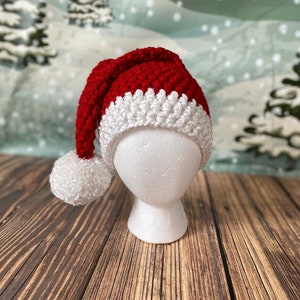 May include: A red and white crocheted Santa hat with a white pom-pom on top. The hat is on a white styrofoam head.