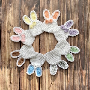 Op de afbeelding: Een set van negen gehaakte konijnenmutsen in verschillende pastelkleuren, gerangschikt in een cirkel op een houten achtergrond.