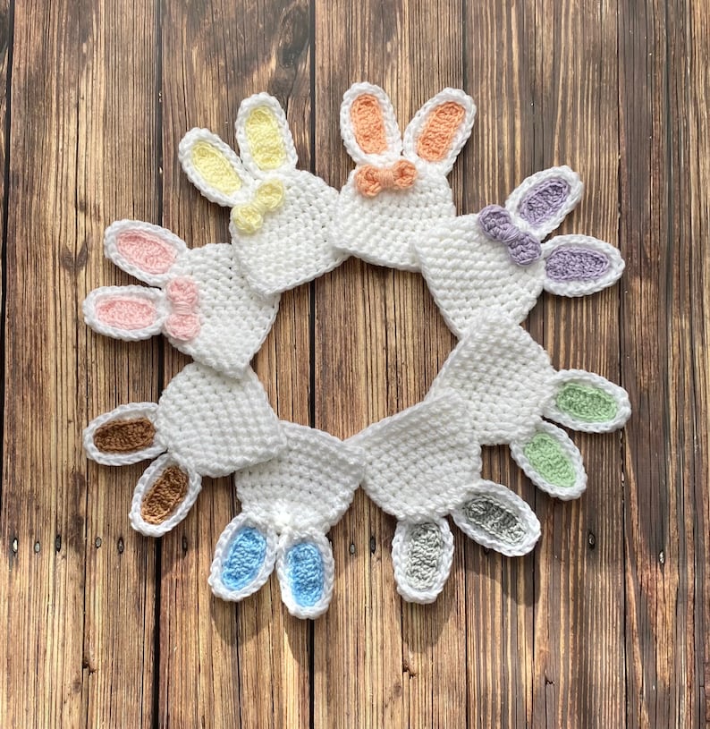 Op de afbeelding: Een set van negen gehaakte konijnenmutsen in verschillende pastelkleuren, gerangschikt in een cirkel op een houten achtergrond.
