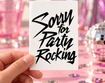 May include: A rectangular white card featuring the black text Sorry for Party Rocking in a bold, stylized, angular font. The card is held upright against a blurred background of pink party decorations and a small silver disco ball.