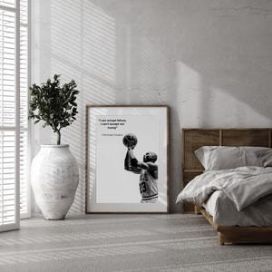 May include: Black and white framed print featuring Michael Jordan shooting a basketball. The print includes the quote "I can accept failure, I can't accept not trying" by Michael Jordan. The print is displayed in a room with a bed and a decorative plant.