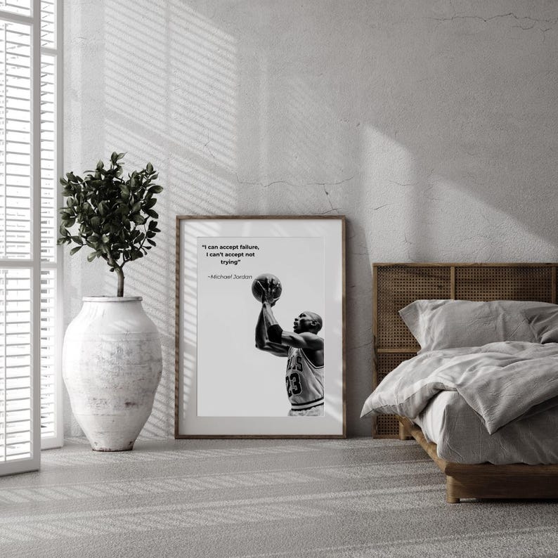 May include: Black and white framed print featuring Michael Jordan shooting a basketball. The print includes the quote "I can accept failure, I can't accept not trying" by Michael Jordan. The print is displayed in a room with a bed and a decorative plant.
