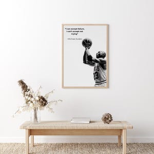 May include: Black and white framed print featuring Michael Jordan shooting a basketball. The print includes the quote "I can accept failure, I can't accept not trying" by Michael Jordan. The image is displayed above a wooden bench.