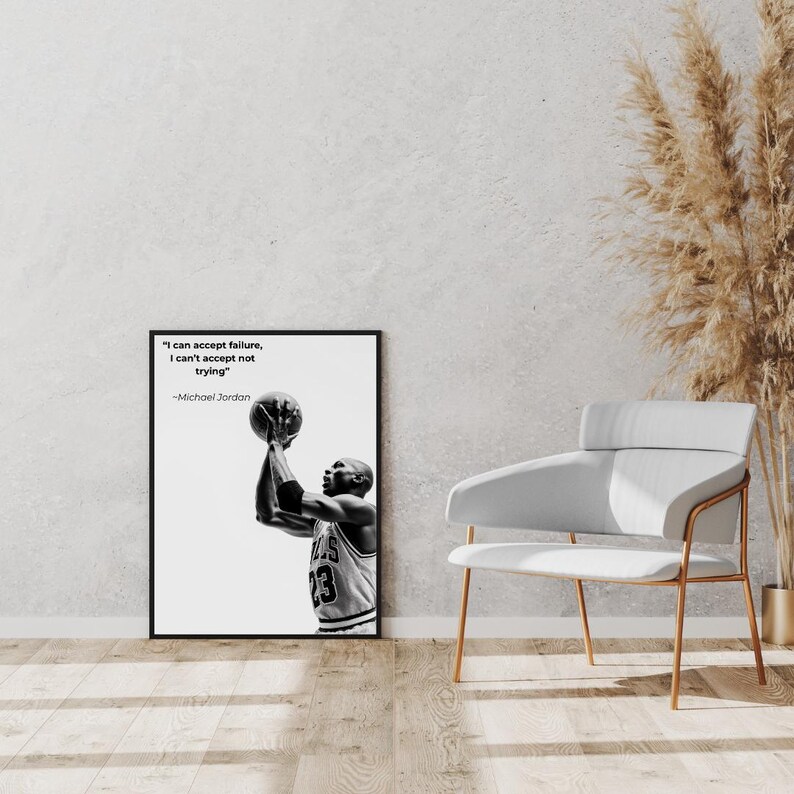 May include: Black and white framed print featuring Michael Jordan shooting a basketball. The print includes the quote "I can accept failure, I can't accept not trying" by Michael Jordan. The image is displayed on a wooden floor.
