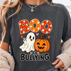 Op de afbeelding: Een antracietgrijs t-shirt met een afbeelding met de tekst BOO TO BULLYING. Het ontwerp bevat een wit spookje dat een vredesteken maakt en een oranje pompoen. Het woord BOO staat in grote oranje letters met witte stippen.