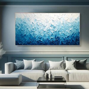 May include: Large abstract painting with a gradient of blue hues, from deep indigo to white. The textured artwork features thick brushstrokes, creating a sense of depth and movement. The framed canvas is displayed above a modern sofa.