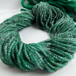 May include: A bundle of emerald green square-cut beads. The beads are strung together, forming a thick, twisted strand. A green tassel is visible at the top. The beads are a vibrant, saturated green color, and the cut of the beads gives them a faceted appearance.