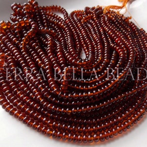 May include: A close-up of a strand of dark brown glass beads. The beads are round and have a smooth, polished finish. The strand is coiled and arranged in a spiral pattern.