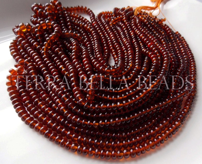 May include: A close-up of a strand of dark brown glass beads. The beads are round and have a smooth, polished finish. The strand is coiled and arranged in a spiral pattern.