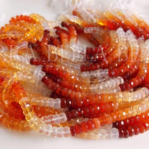 May include: Strands of faceted gemstone beads in shades of orange, red, and clear. The beads are arranged in a circular pattern, creating a gradient effect. The beads are likely for jewelry making.