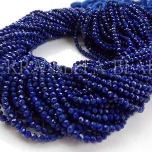 May include: A strand of deep blue faceted lapis lazuli beads. The beads are small and uniform in size, and they are strung on a thin thread. The beads are arranged in a circular pattern, and they are all facing the same direction.