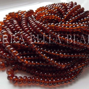 May include: A close-up of a pile of small, round, brown glass beads. The beads are arranged in a spiral pattern and have a glossy finish.