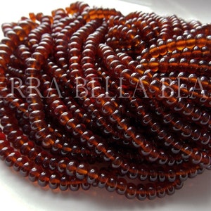 May include: A close-up of a strand of dark brown glass beads. The beads are small and round, and they are arranged in a spiral pattern. The beads are all the same size and shape, and they have a smooth, glossy finish.