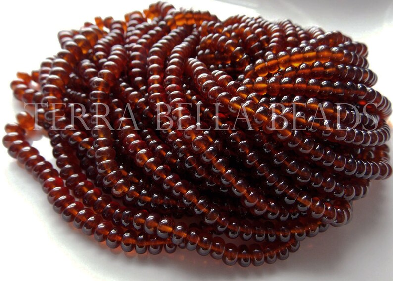 May include: A close-up of a strand of dark brown glass beads. The beads are small and round, and they are arranged in a spiral pattern. The beads are all the same size and shape, and they have a smooth, glossy finish.