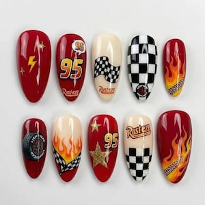 May include: A set of ten almond-shaped press-on nails featuring a racing theme. Designs include red backgrounds with yellow lightning bolts, the number 95, Rust-eze logos, black and white checkered patterns, orange flames, and gold glitter stars.