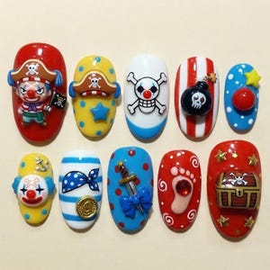 May include: A set of ten pirate-themed nail art designs. Each nail features a different design, including a clown, skull and crossbones, a bomb, a treasure chest, and other pirate-related elements. The nails are painted in various colors, including red, yellow, blue, and white.