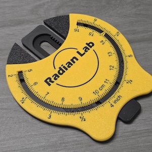 May include: A yellow Radian Lab tool with black detailing. It has curved measurement scales in inches and centimetres, with the text "Radian Lab" printed on the face. The tool measures approximately 10 cm (4 inches) in length.