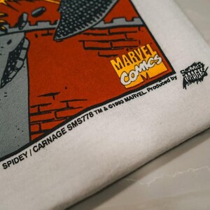 May include: A white fabric surface featuring a printed graphic with a red brick wall, a grey structure, and the yellow Marvel Comics logo. Text reads: SPIDEY / CARNAGE SMS778 TM & &copy;1993 MARVEL. Produced by COMIC IMAGES. The print includes a black textured shape.
