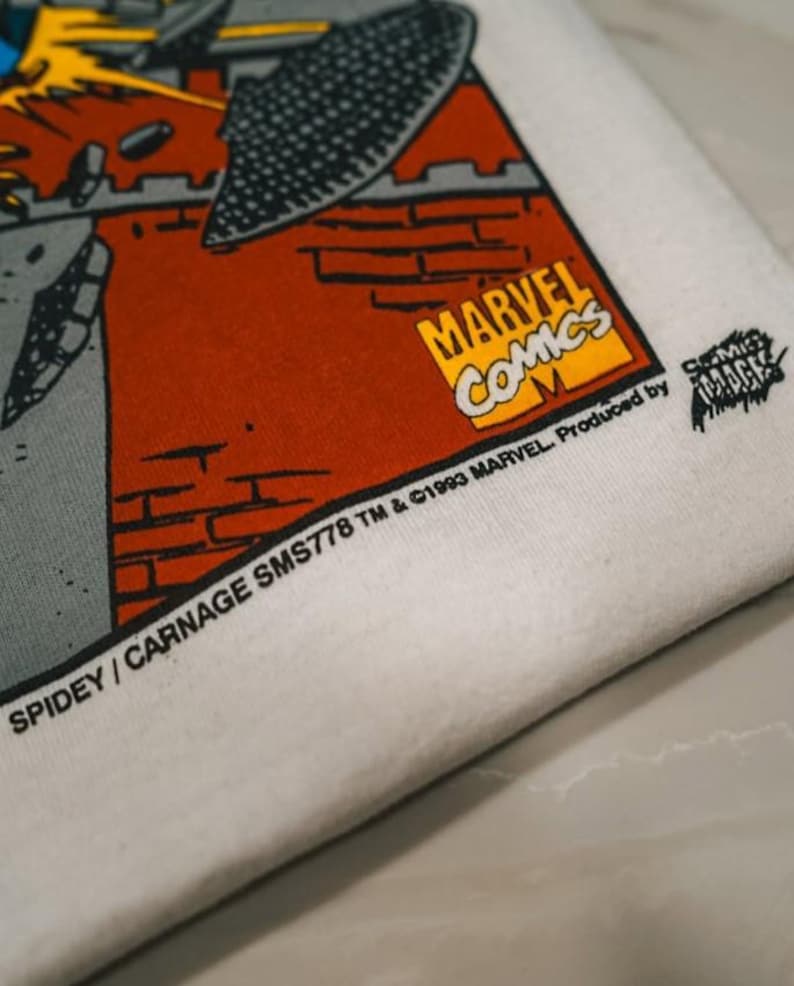 May include: A white fabric surface featuring a printed graphic with a red brick wall, a grey structure, and the yellow Marvel Comics logo. Text reads: SPIDEY / CARNAGE SMS778 TM & &copy;1993 MARVEL. Produced by COMIC IMAGES. The print includes a black textured shape.