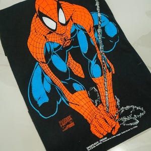 May include: A black t-shirt featuring a graphic print of Spider-Man in a crouching pose with orange and blue colors. The print includes the text Marvel Comics, Spider-Man, SMS680, TM & &copy;1991 MARVEL Produced by Comic Images, Saddle Brook, N.J. 07662.