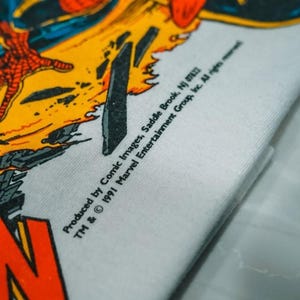 May include: A white t-shirt featuring a vibrant comic book graphic with red, yellow, and black colors. The print includes the text: Produced by Comic Images, Saddle Brook, NJ 07662 TM & &copy; 1991 Marvel Entertainment Group, Inc. All rights reserved.