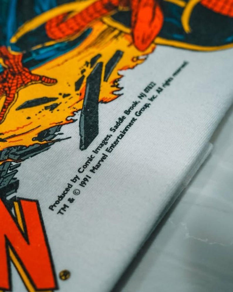 May include: A white t-shirt featuring a vibrant comic book graphic with red, yellow, and black colors. The print includes the text: Produced by Comic Images, Saddle Brook, NJ 07662 TM & &copy; 1991 Marvel Entertainment Group, Inc. All rights reserved.
