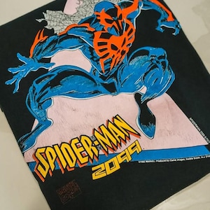Op de afbeelding: Een zwart t-shirt met een grafische print van Spider-Man 2099 in blauw en oranje. Het personage staat in een dynamische pose boven de gele en oranje tekst die SPIDER-MAN 2099 leest. De print bevat de Marvel copyright-tekst.
